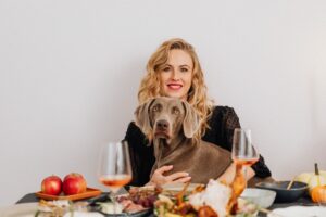 A smiling woman holding her dog at a cozy dinner table setting, enjoying a festive atmosphere.